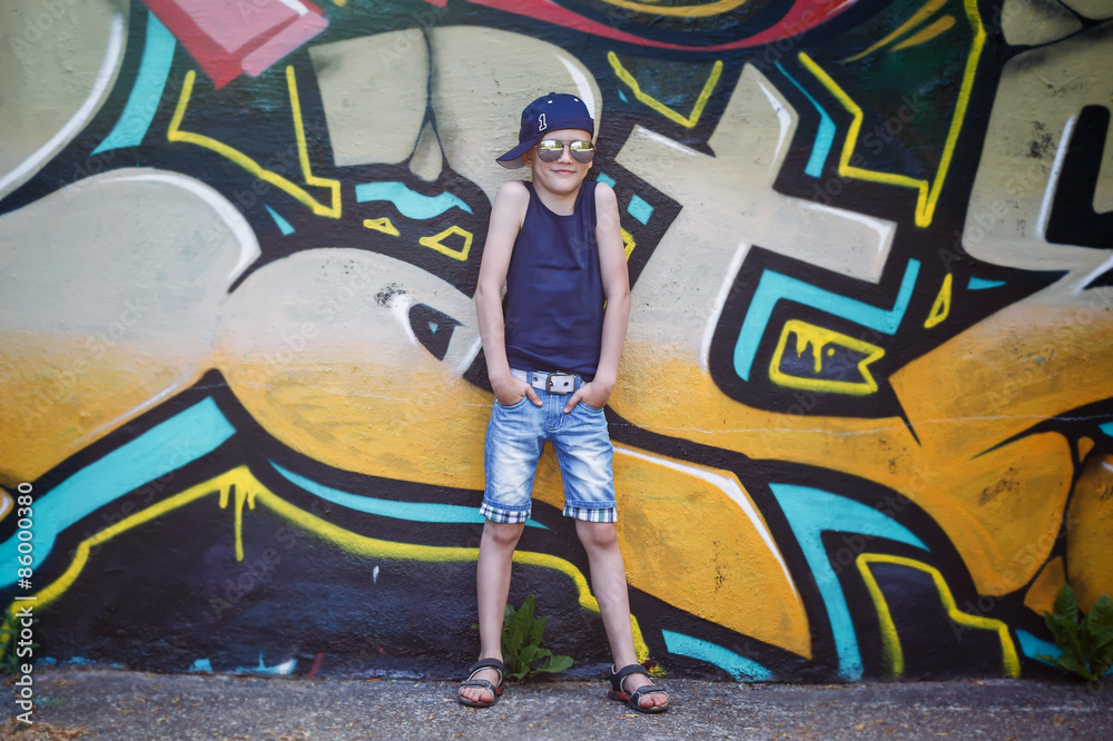 Fototapeta premium Fashionable little boy in sunglasses and cap.Graffiti background