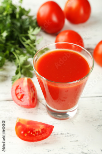 Glass of tomato juice on white wooden background