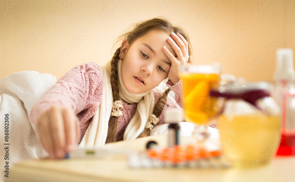 sick girl lying in bed and taking thermometer from bedside table sick girl lying in bed and taking thermometer from bedside table
