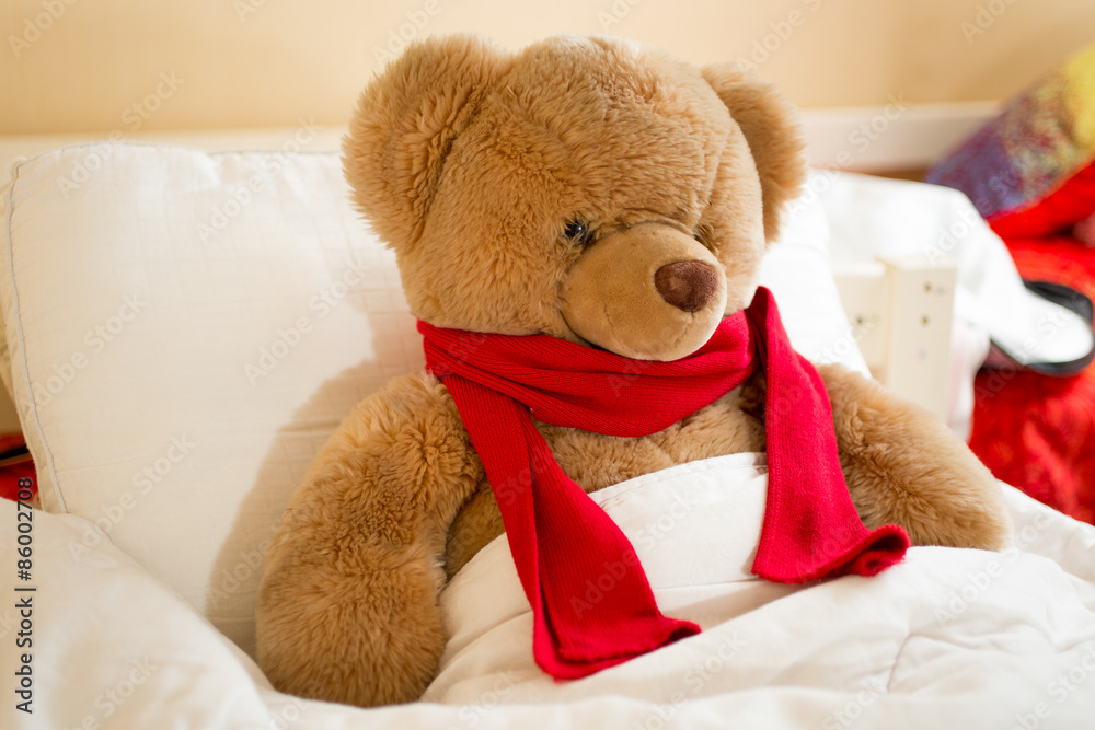 Closeup of brown teddy bear in red scarf lying in bed