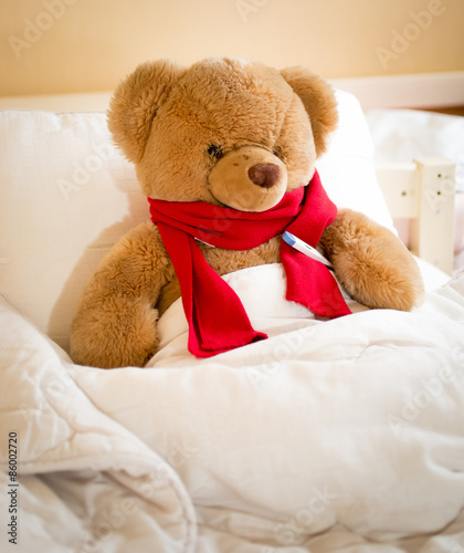 Closeup of teddy bear in red scarf lying in bed