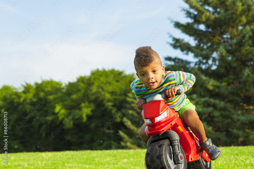 Cute afro boy on the red motorbike toy. Cute afro boy on the red motorbike toy.
