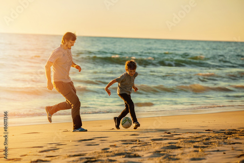 Happy father and son play soccer or football on the beach in