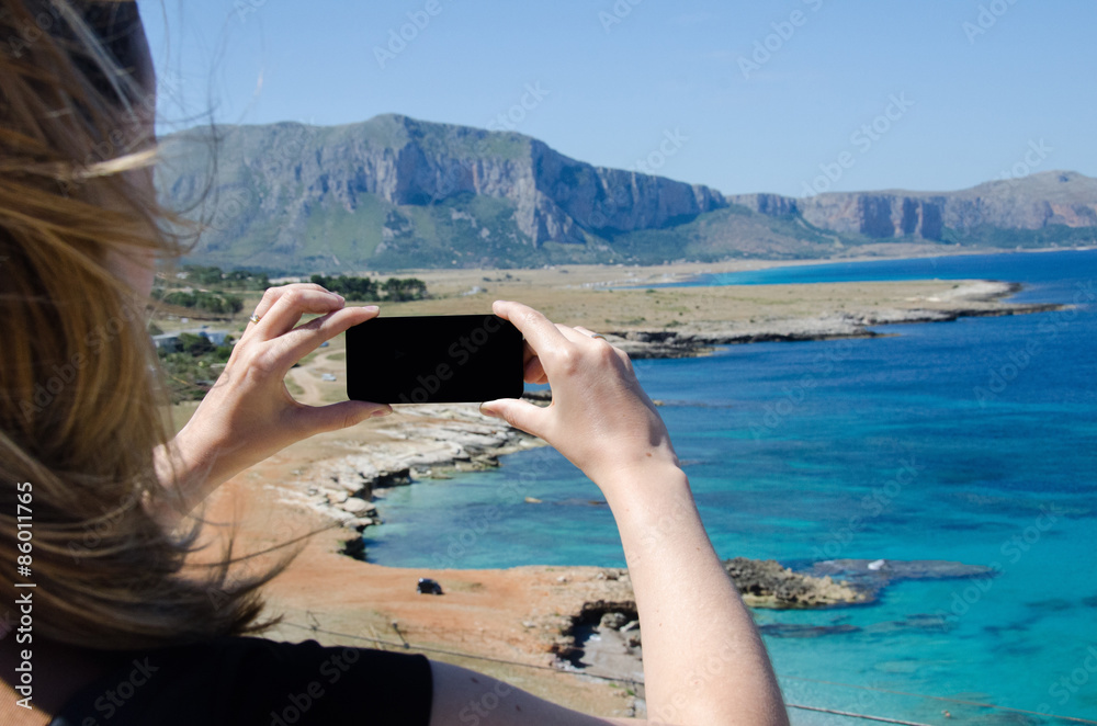 Girl takes picture with smartphone on a bay with panoramic seaviews in Sicily Italy 