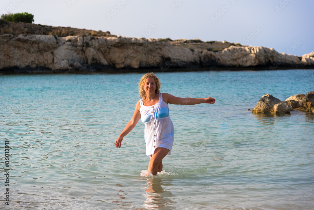 Attractive blond hair girl in white dress walking in sea