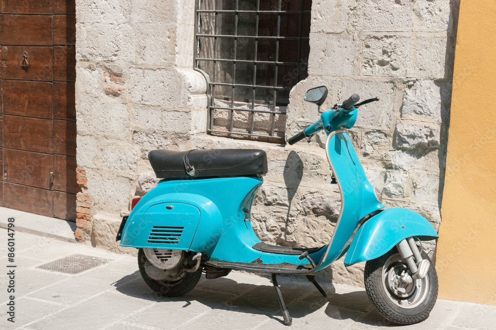 Bright aqua motor scooter parked in Italian village street.