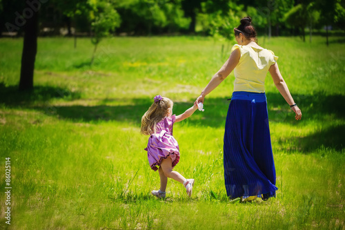 Little girl together with mother run and play on a grass in the