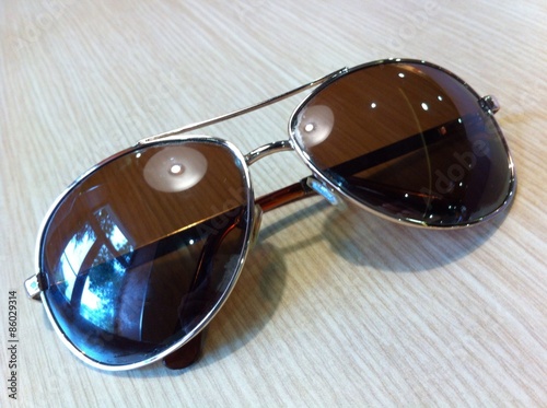 Sunglasses close-up  which reflect the window and lamp on a wooden table