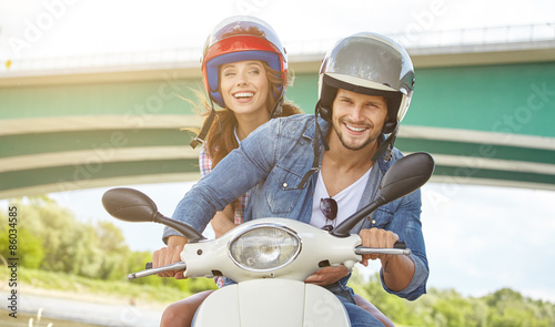 Foto Happy young couple riding a scooter in the city on a sunny day