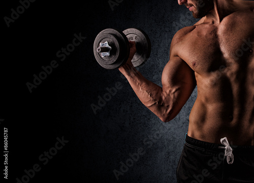 Handsome muscular man working out with dumbbells over black back