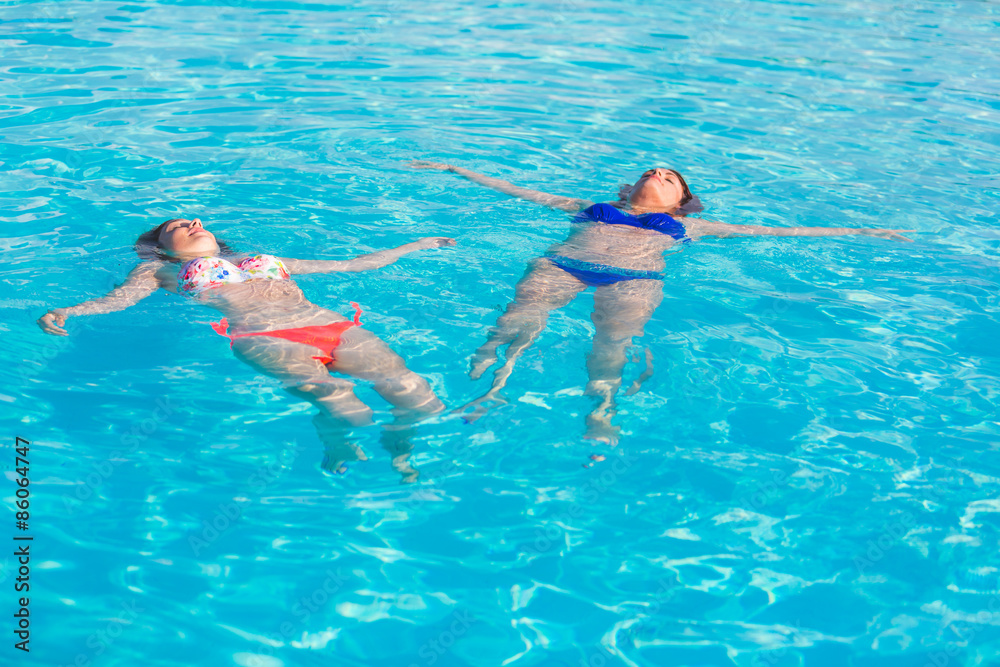 Two beautiful women lying on swimming pool water surface