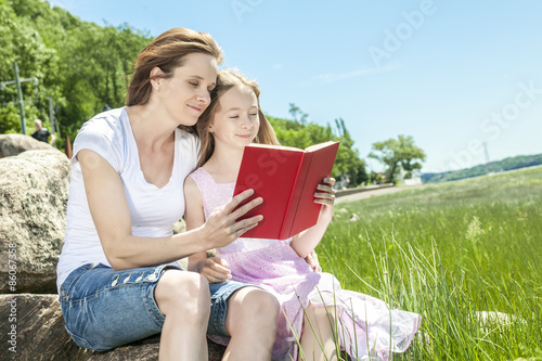 Little girl with mother reading a book in a summer park
