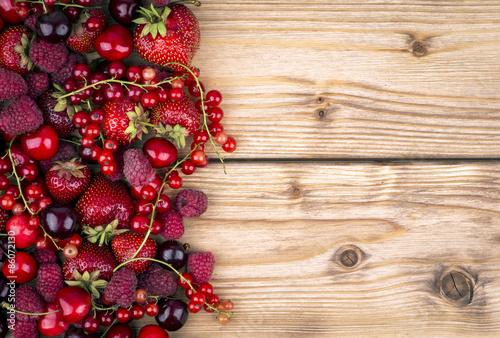 Strawberries, currants, raspberries and cherries on the wooden background.