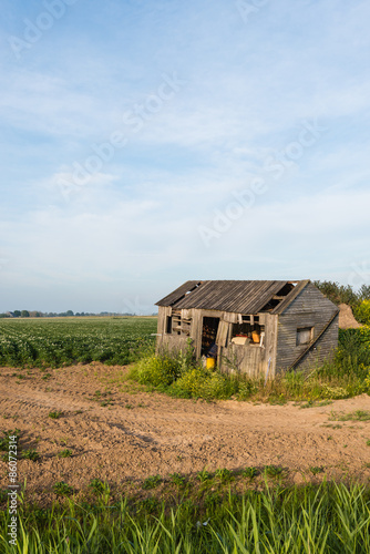 Old dilapidated small wooden barn beside a potato field