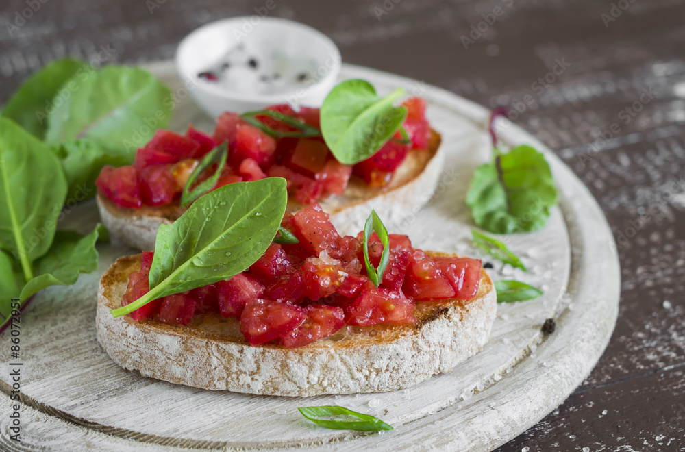 bruschetta with tomatoes and fresh spinach on a light wooden background