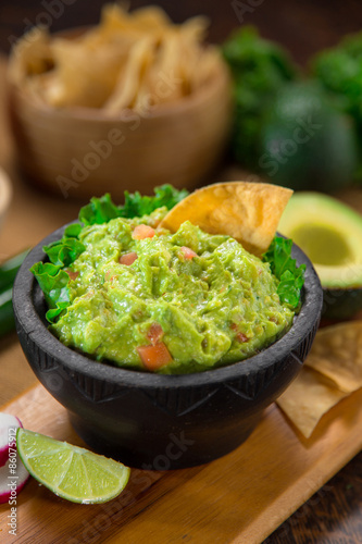 Guacamole and chips on a wood cutting board vertical shot restaurant style serving