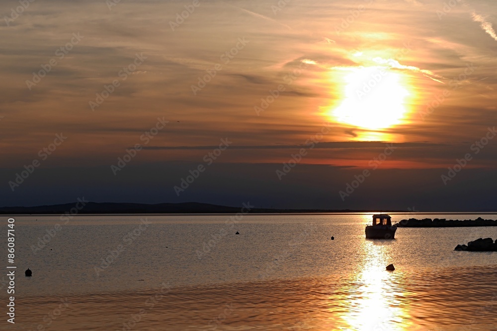 Sunset with small ship, buoys and rocky molo in Croatia