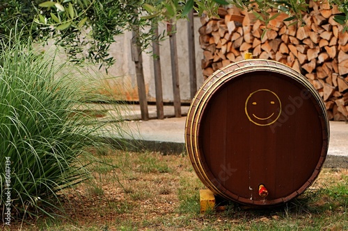 Wooden wine barrel on lawn with yellow smiley picture and pile o wood in background photo