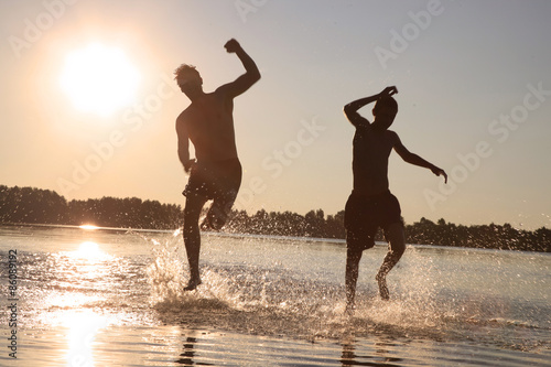 Glückliche junge Menschen laufen und springen am See beim Sonnenuntergang