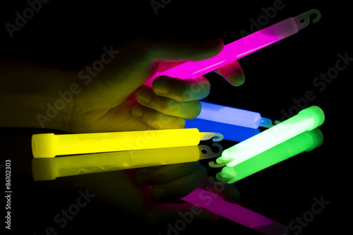 A hand holding pink glow stick,with other color glow sticks on a dark background