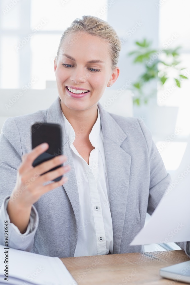 Smiling businesswoman sending a text at her desk Smiling businesswoman sending a text at her desk