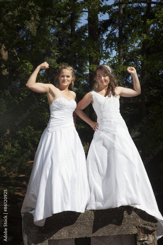 picture of two brides standing on concrete object in nature surr