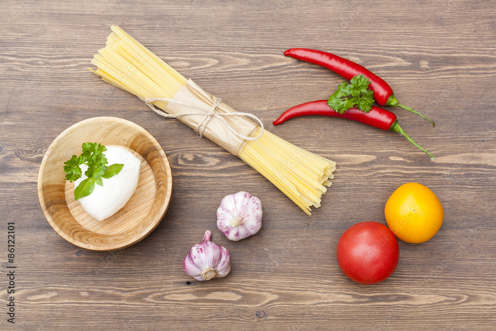 Noodles in paper tied with a rope, a wooden bowl mozzarella, fresh herbs and fresh vegetables on wooden table Noodles in paper tied with a rope, a wooden bowl mozzarella, fresh herbs and fresh vegetables on wooden table