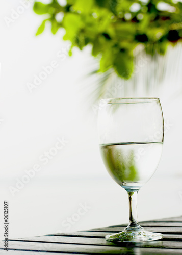 Glass of pure water on a dark table on the beach with a palm tre