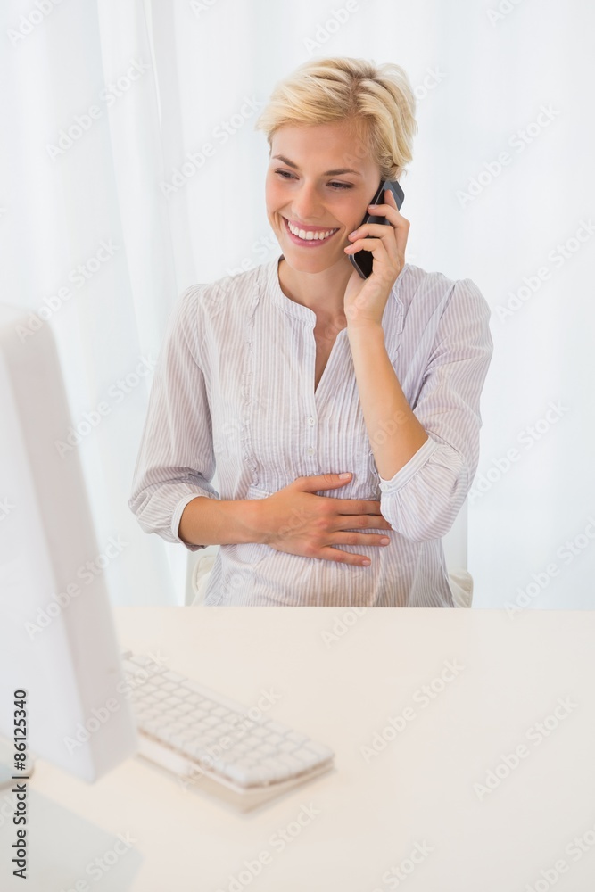 Smiling blonde woman using computer and phoning 