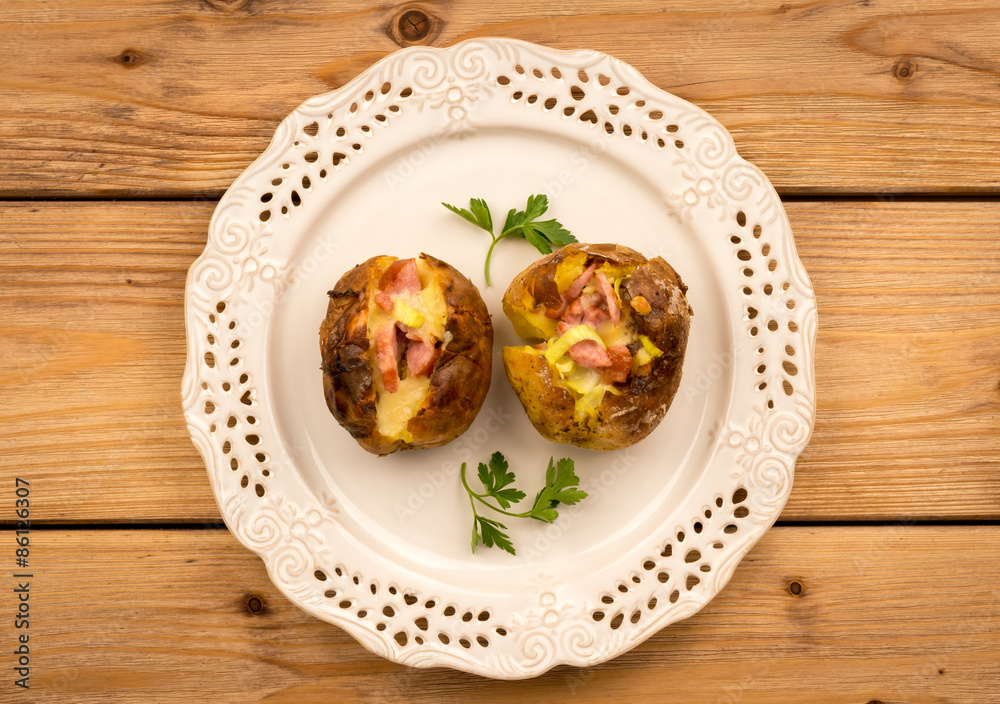 Baked potato with ham and cheese on the plate on the wooden background,