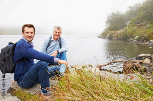 Father and young adult son sitting by a lake