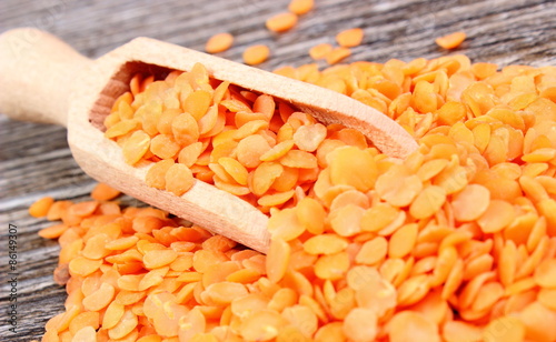 Heap of red lentil with spoon on wooden background