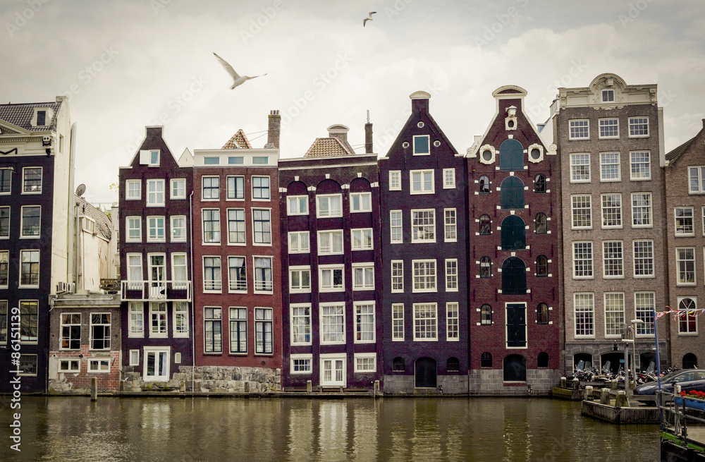 Row of traditional, old crooked houses along canal in Amsterdam, Holland with cloudy sky and seagulls