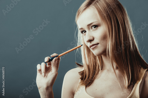  blonde girl thinking holds pen on gray background