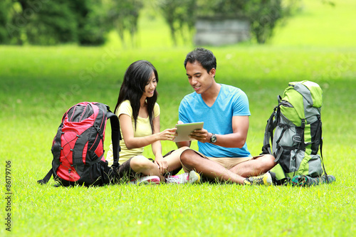 Young asian couple standing on the park holding a tablet pc show