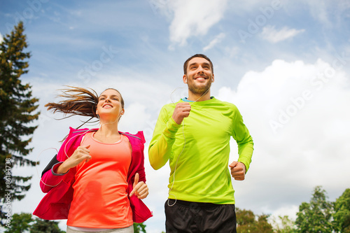 smiling couple with earphones running outdoors