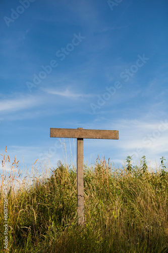 Wooden old road sign pole and blue sky with clouds on background with green grass