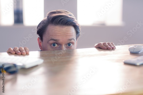 Nervous businessman peeking over desk