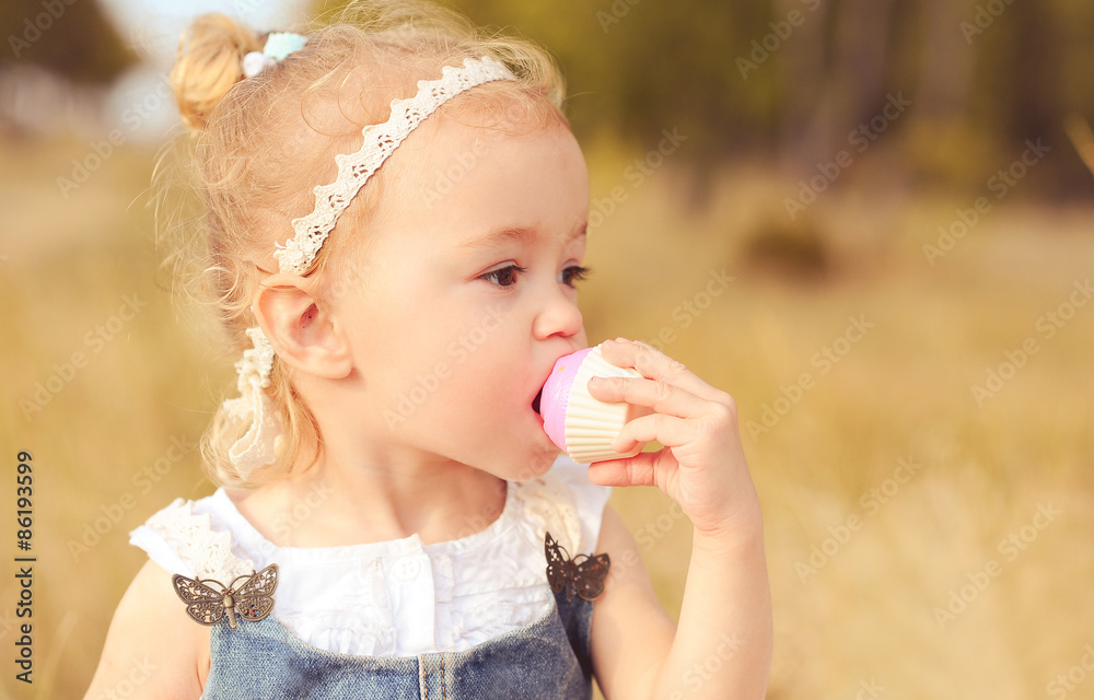 Baby girl 2-3 year old eating cupcake outdoors. Wearing stylish clothes. Baby girl 2-3 year old eating cupcake outdoors. Wearing stylish clothes.