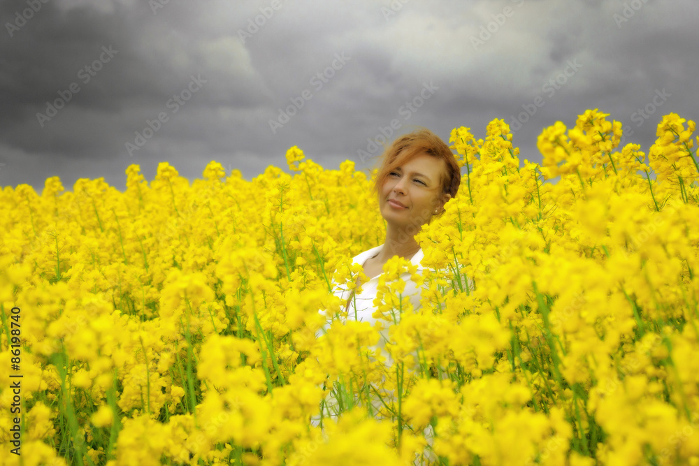 Young happy woman is walking in canola field under storm clouds Young happy woman is walking in canola field under storm clouds