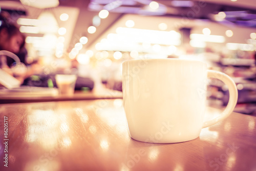 Vintage filter  White coffee cup on wood table with blurred cafe