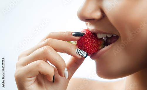 Macro view of a pretty young female eating fresh strawberry
