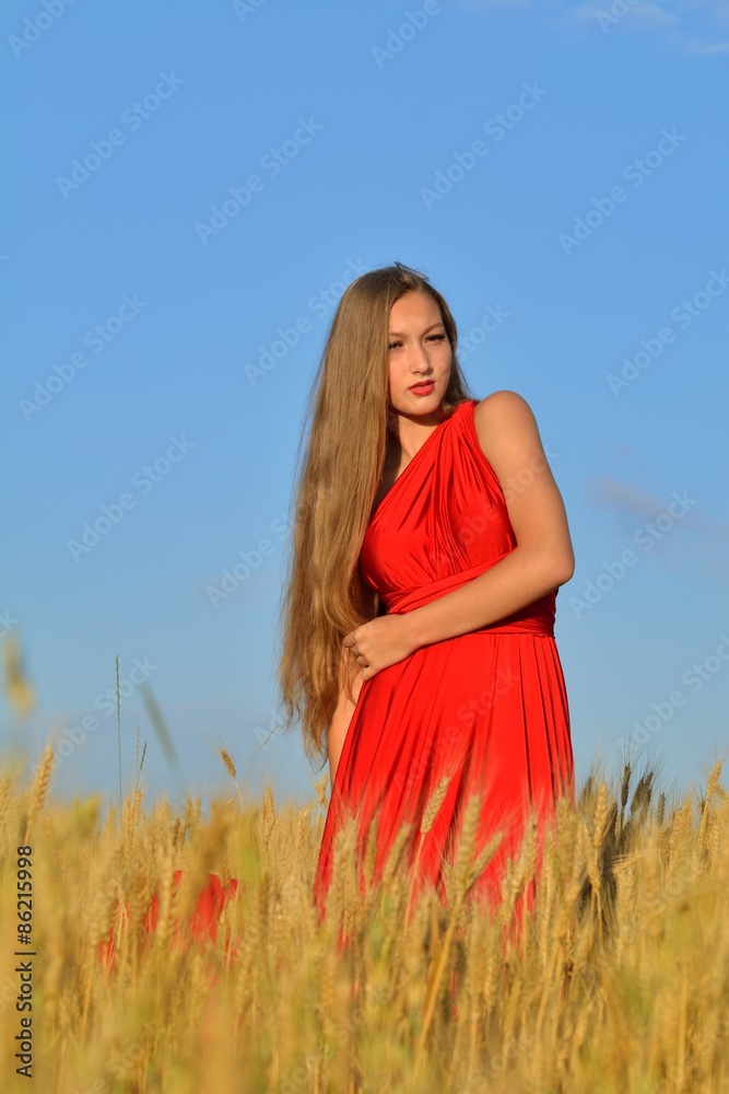 Obraz premium Young beautiful woman and a red dress in a wheat field