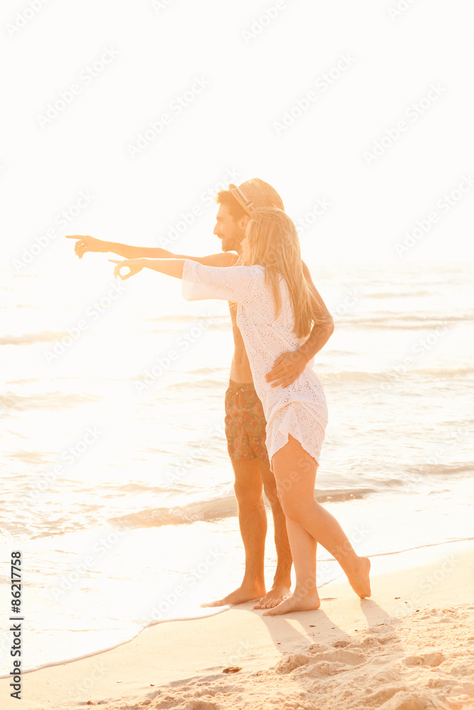 Sunset, sandy beach, a loving couple walks embraced on the deserted beach at sunset during a day at the beach on vacation. The loving couple shows something with his hands in the sea