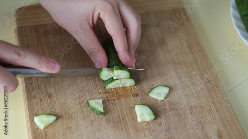 Hand cutting cucumber on cutting board with sharp knife photo