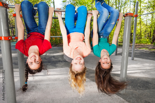 Three girls hanging upside-down on brachiating bar photo