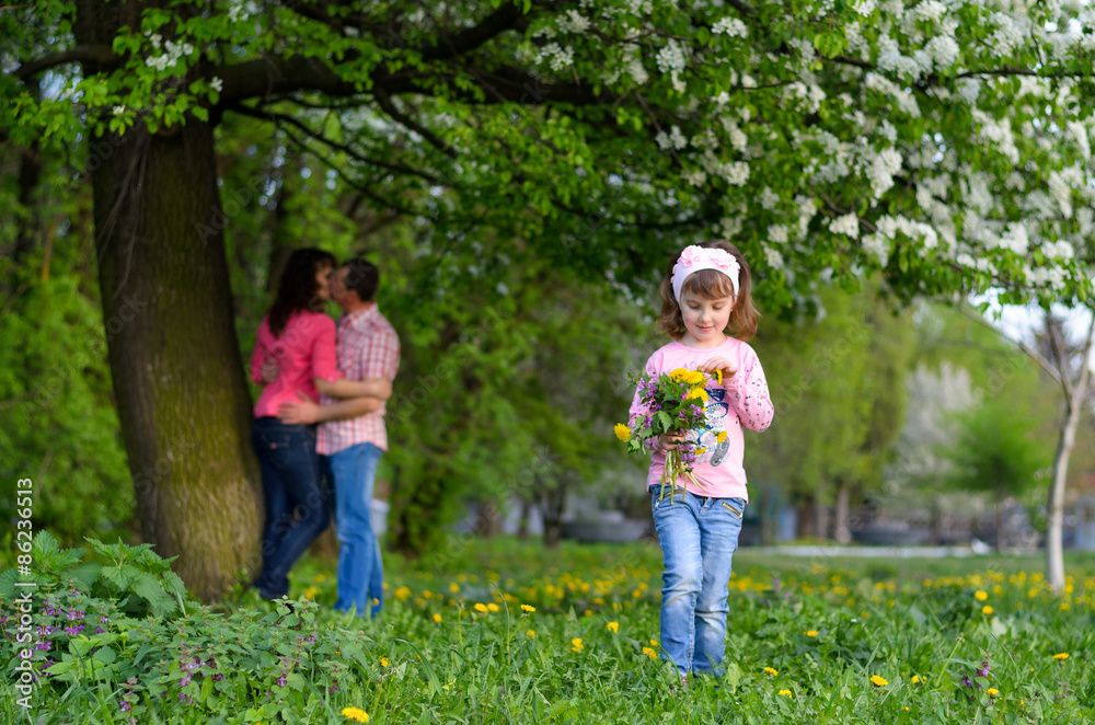 a girl collects the field flowers in a bouquet sits near parents