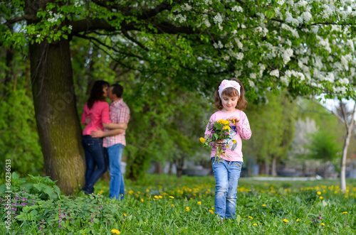 a girl collects the field flowers in a bouquet sits near parents