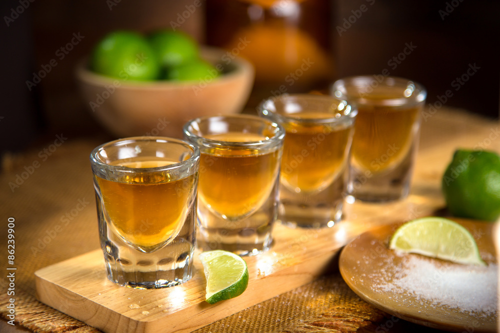Four shot glasses with tequila bottle and bowl of limes with salt at a bar  Stock-Foto | Adobe Stock
