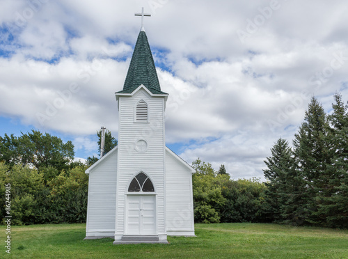 quaint little country church sitting in a green meadow surrounded by trees in the summer time